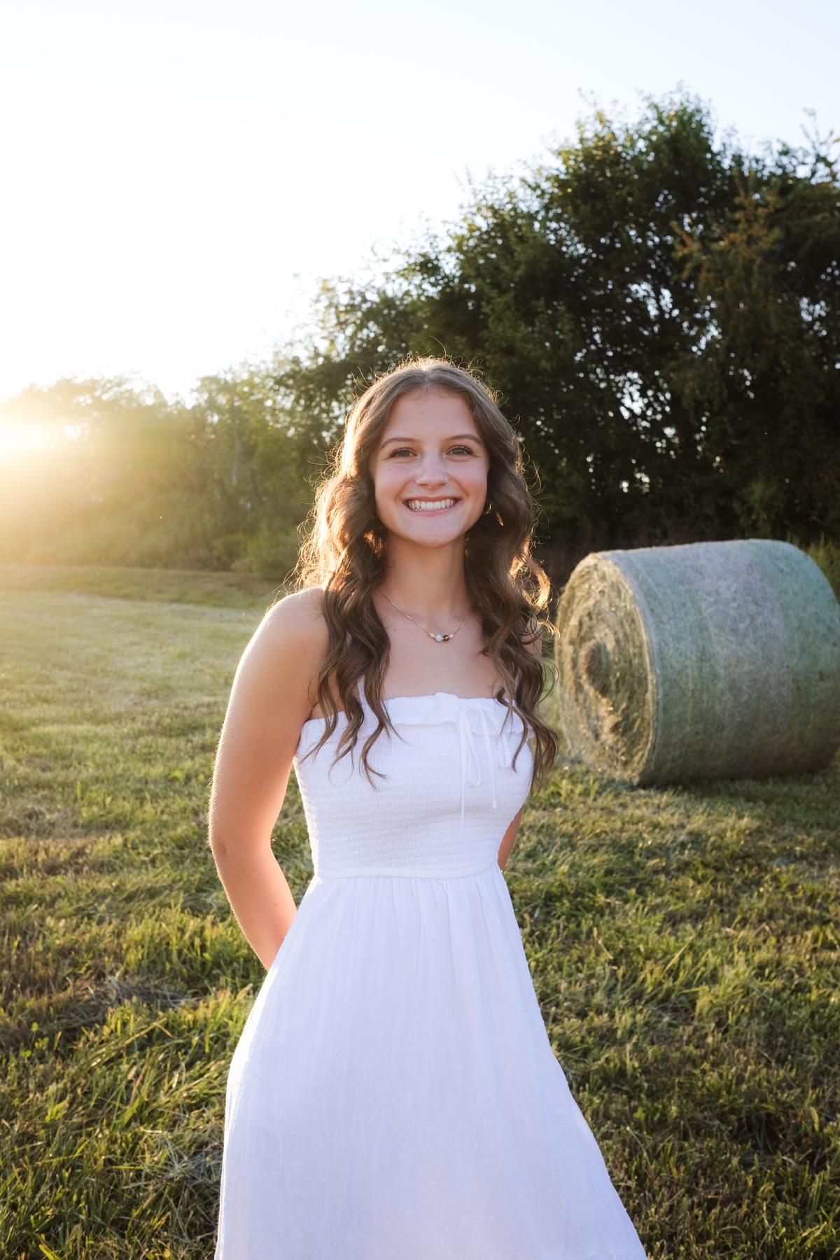 Senior portrait by a hay bale at sunset