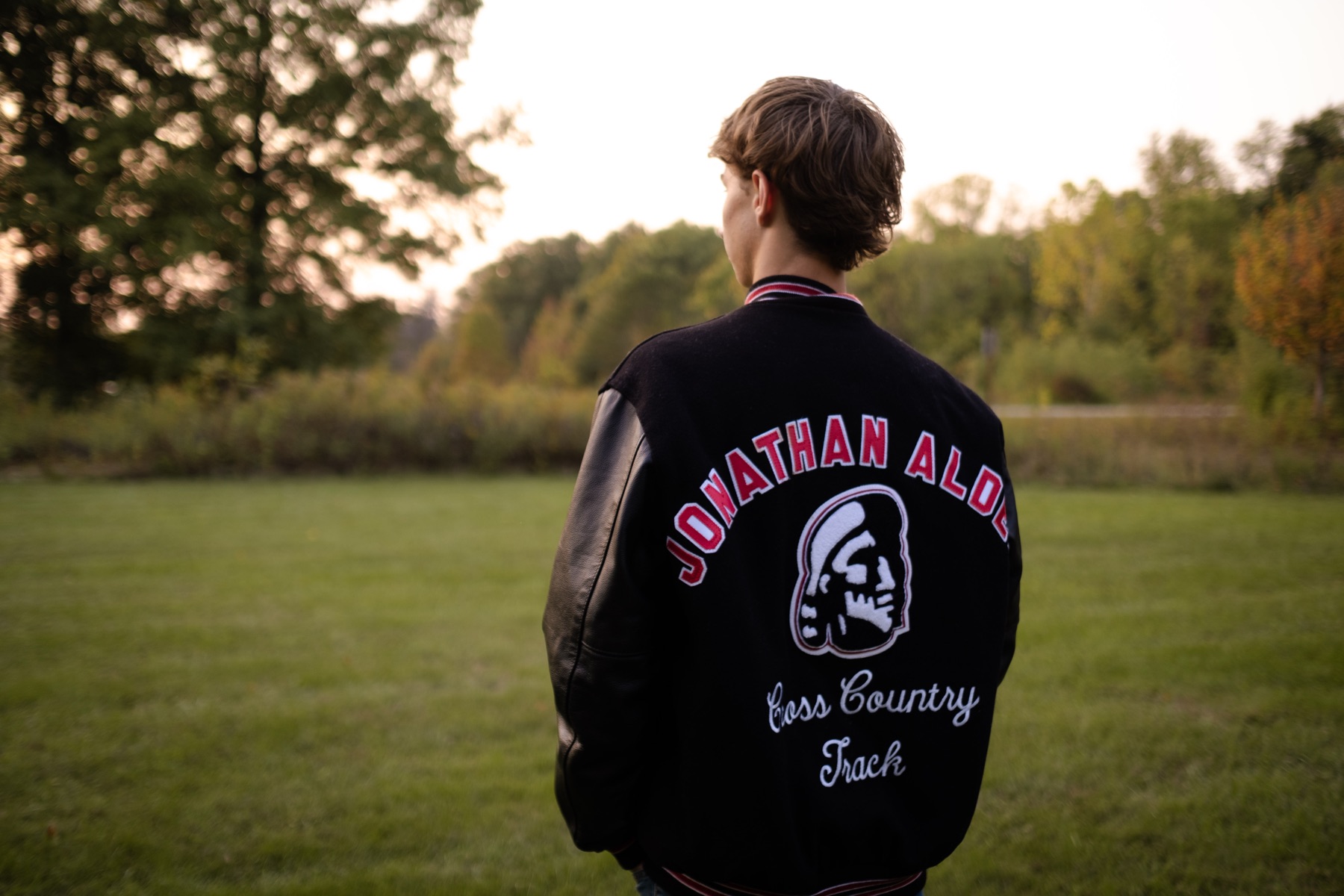 Senior portrait in a letterman jacket at sunset
