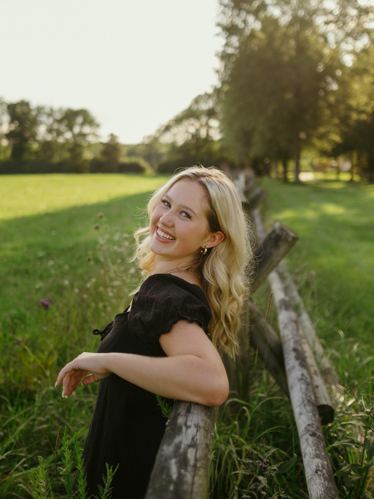 Senior portrait leaning against a wooden fence in a black dress