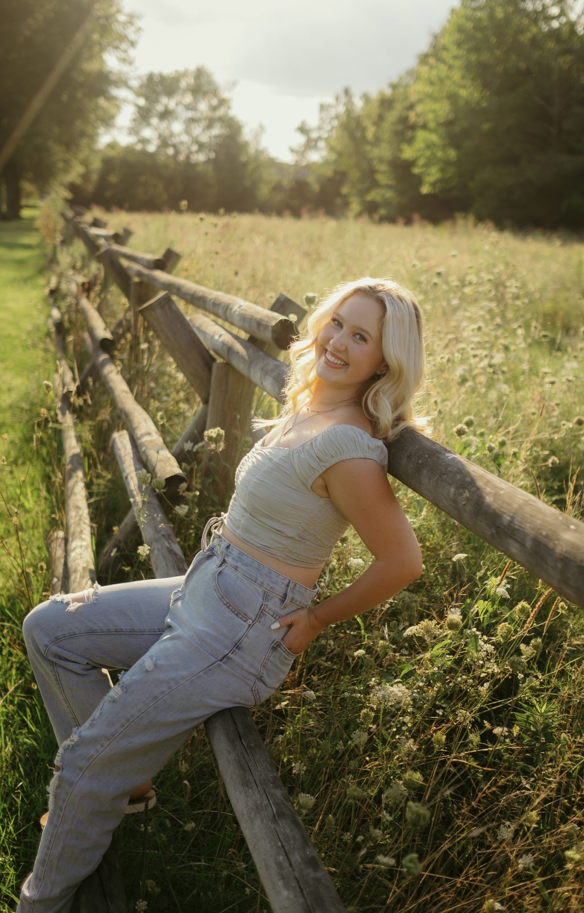 Senior portrait sitting on a fence rail in a sunlit field